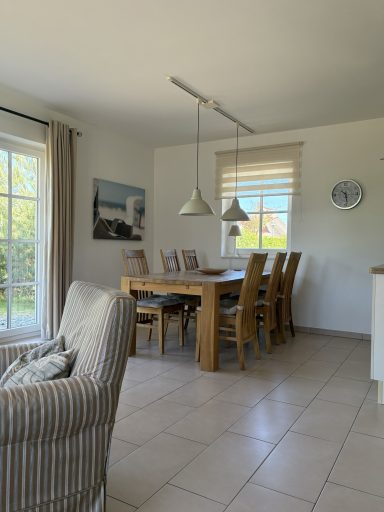 Heller, neutrales Esszimmer mit Holzstuhl und Tisch, großem Fenster und Pendelleuchten.